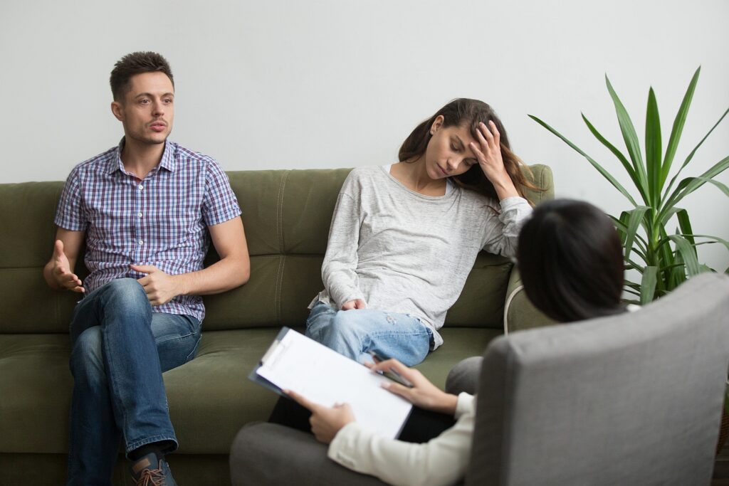 Husband talking, explaining point view in psychologist or relationship expert office, wife being indifferent.